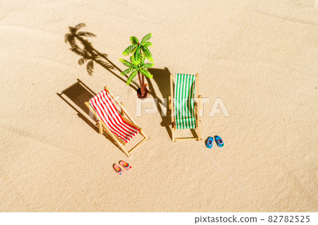 Aerial view of two deck chair, sunbed, lounge, flip flops, palm tree on sandy beach. Summer and travel concept. Minimalism Aerial view of two deck chair, sunbed, lounge, flip flops, palm tree on sandy beach. Summer and travel concept. Minimalism 82782525