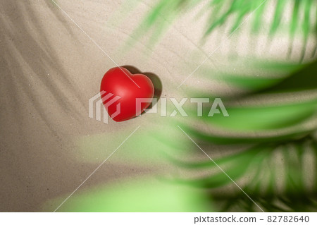 Red heart on sandy tropical beach under branches of palm and shadow palm tree. Valentines day, love. Holiday concept. Creative, background, travel, summer. 82782640