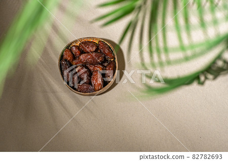 Royal dates fruit in a bowl of coconut on the sand beach under palm branches and leaves shadow. Royal dates fruit in a bowl of coconut on the sand beach under palm branches and leaves shadow. 82782693