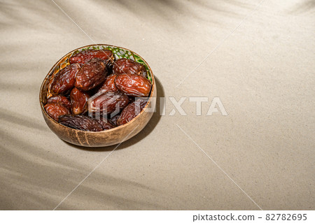 Royal dates fruit in a bowl of coconut on the sand beach under palm branches and leaves shadow. 82782695