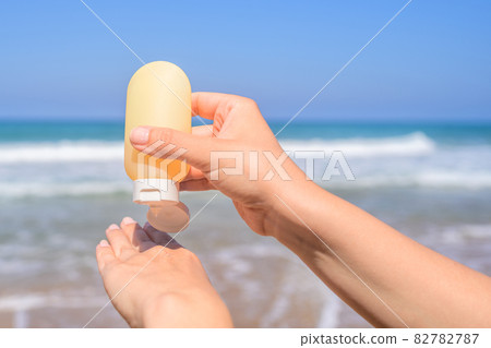 Woman applying sunscreen on skin of hand on a beach of coastline sea. Female relaxation at summer vacation. Back view 82782787
