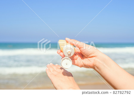 Woman applying sunscreen on skin of hand on a beach of coastline sea. Female relaxation at summer vacation. Back view 82782792