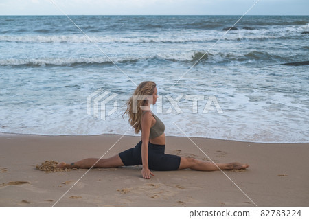 Fit blonde girl do sport gymnastics workout near the sea. Portrait of gorgeous sport woman doing stretching exercise outdoors. Healthy lifestyle 82783224
