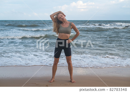 Sporty fit active young blonde caucasian woman in sportswear stretching neck muscles on the beach. Healthy lifestyle concept, ocean view, beach  82783348