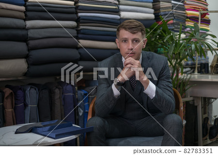 Man in grey suit and watches sitting in atelier and looking at camera with copy space. High quality photo 82783351