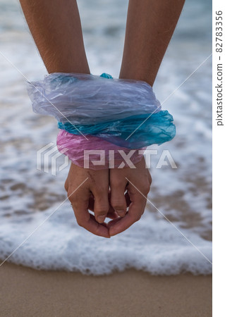 Woman hands wrapped in blue, pink and white plastic bags on the beach. Sea on the background. Concept of stop plastic pollution, plastic free Woman hands wrapped in blue, pink and white plastic bags on the beach. Sea on the background. Concept of stop plastic pollution, plastic free 82783356