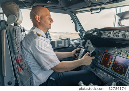 Confident pilot sitting in the cockpit and holding the steering wheel Confident pilot sitting in the cockpit and holding the steering wheel 82784174