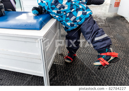 Close-up detail view of little kids leg wearing blue plastic rental skating boots standing on non-slip rubber soft mat in dressing room of skating rink. Healthy children recreation leisure activity 82784227