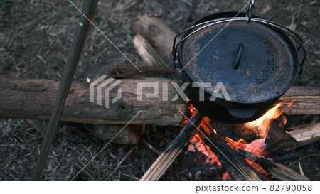 Camping outdoors in nature. Cooking pot hanging over a campfire on a tripod at a tourist camp, a bowler on a bonfire by firewoods. Preparing dinner in a pot in the forest. Nice camping background 82790058