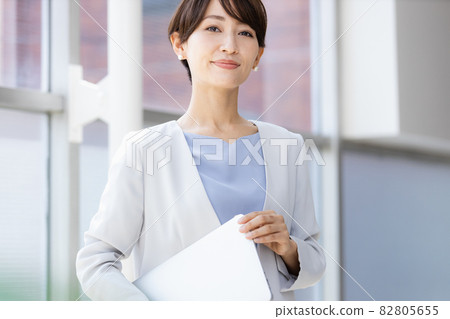 A business woman standing by the window holding a laptop A business woman standing by the window holding a laptop 82805655