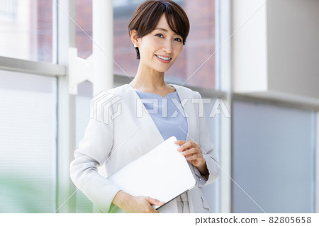 A business woman standing by the window holding a laptop 82805658