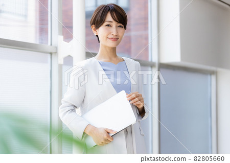 A business woman standing by the window holding a laptop 82805660