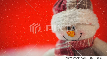 Image of snow falling against christmas snowman on red 82808375