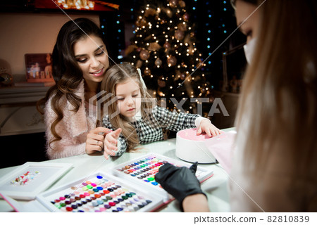 Mom and daughter are choosing the color of nail polish in a beauty salon before Christmas. Mom and daughter are choosing the color of nail polish in a beauty salon before Christmas. 82810839