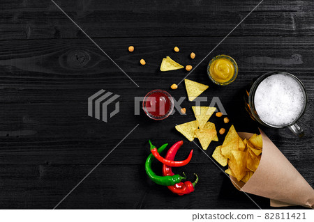 Top view of tortilla chips with sauce, glass of beer and red chili pepper on black wooden background 82811421