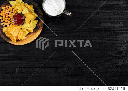 Lager beer and snacks on black wooden table. Nuts, chips. Top view with copyspace Lager beer and snacks on black wooden table. Nuts, chips. Top view with copyspace 82811426