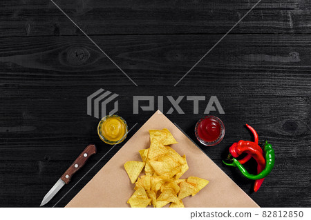 Top view of tortilla chips with sauce and red chili pepper on black wooden background 82812850