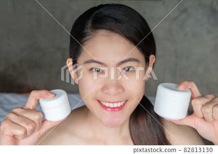 Portrait of young Asian woman holding packaging cream container in her hand and looking to camera. Conceptual of beauty and cosmetic. Portrait of young Asian woman holding packaging cream container in her hand and looking to camera. Conceptual of beauty and cosmetic. 82813130
