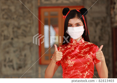 Beautiful young Asian woman in red Chinese dress traditional cheongsam qipao wear protect mask for healthcare with gesture showing thumb up or double like (New normal and Chinese new year concept) Beautiful young Asian woman in red Chinese dress traditional cheongsam qipao wear protect mask for healthcare with gesture showing thumb up or double like (New normal and Chinese new year concept) 82813403