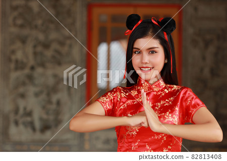 Beautiful young Asian woman in red Chinese dress traditional cheongsam qipao with gesture of congratulation and happy smiling face, she standing in front of the ancient wall (Chinese new year concept) Beautiful young Asian woman in red Chinese dress traditional cheongsam qipao with gesture of congratulation and happy smiling face, she standing in front of the ancient wall (Chinese new year concept) 82813408