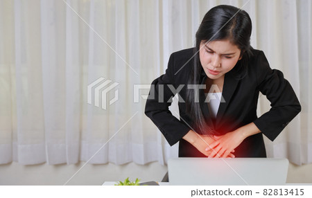 Young asian stressed businesswoman feeling pain or having problem with part of body menstrual pain or stomachache while working on computer. Office syndrome concept 82813415
