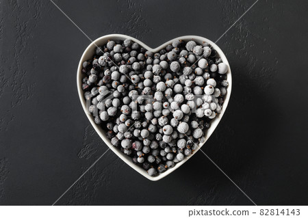 Frozen black currant in plate shaped as heart on a black background. View from above. 82814143