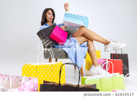 Close-up surprised young girl after shopping at black friday sales. Model with lots of bags, colorful bright packages isolated over white studio background. Close-up surprised young girl after shopping at black friday sales. Model with lots of bags, colorful bright packages isolated over white studio background. 82814517