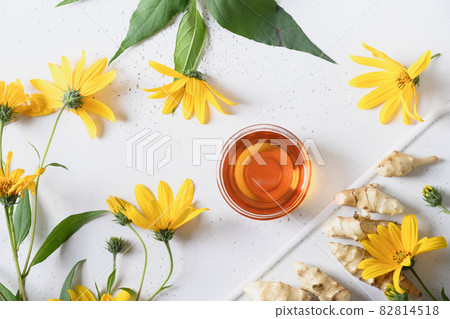 Jerusalem artichoke syrup in bowl, flowers and root. 82814518