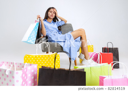 Close up tired beautiful young girl after shopping at black friday sales. Model with lots of bags, colorful bright packages isolated over white studio background. 82814519