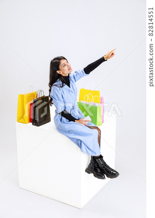 Portrait of young woman with lots of bags, colorful bright packages sitting on huge box isolated over white studio background. Portrait of young woman with lots of bags, colorful bright packages sitting on huge box isolated over white studio background. 82814551