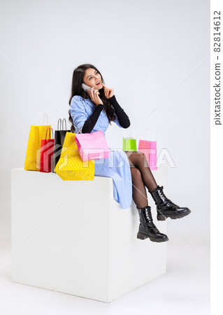 Portrait of young woman with lots of bags, colorful bright packages sitting on huge box isolated over white studio background. Portrait of young woman with lots of bags, colorful bright packages sitting on huge box isolated over white studio background. 82814612