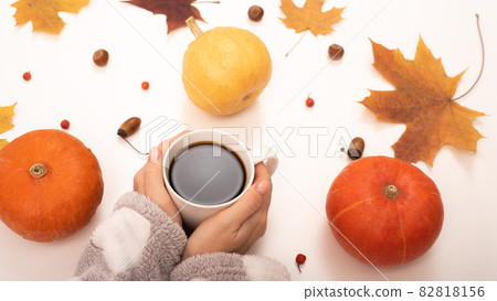 A woman holds a cup of black coffee near the yellow maple leaves of a pumpkin on a white background. Autumn flat lay. 82818156