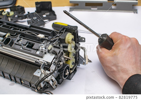the hand of the service center master squeezes a phillips screwdriver near the disassembled gearbox the hand of the service center master squeezes a phillips screwdriver near the disassembled gearbox 82819775