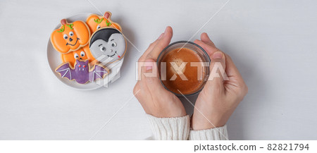 woman hand holding coffee cup during eating funny Halloween Cookies. Happy Halloween day, Trick or Threat, Hello October, fall autumn, Traditional, party and holiday concept 82821794