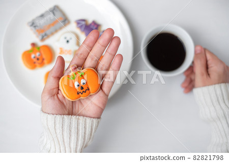 woman hand holding funny Halloween Cookie during drinking coffee. Happy Halloween day, Trick or Threat, Hello October, fall autumn, Traditional, party and holiday concept woman hand holding funny Halloween Cookie during drinking coffee. Happy Halloween day, Trick or Threat, Hello October, fall autumn, Traditional, party and holiday concept 82821798