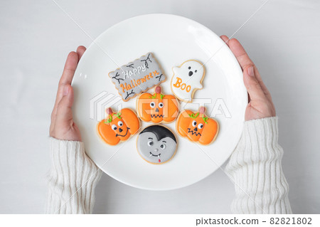 woman hand holding plate of funny Halloween Cookies. Happy Halloween day, Trick or Threat, Hello October, fall autumn, Traditional, party and holiday concept 82821802