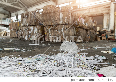 Dump pile of used shreded paper wrap and document against bales of compressed cardboard collected for recycling and reuse at industrial plant or factory. Sustainable materials and environment concept 82822159