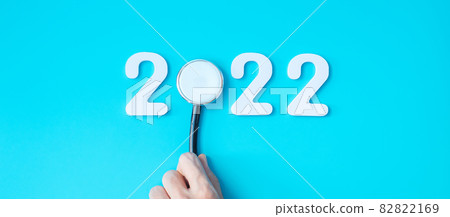 hand holding Stethoscope with 2022 number on blue background. Happy New Year for healthcare, Insurance, Wellness and medical concept hand holding Stethoscope with 2022 number on blue background. Happy New Year for healthcare, Insurance, Wellness and medical concept 82822169