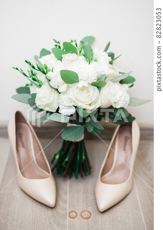 Pair of elegant and stylish bridal shoes with wedding rings and a bouquet of roses and other flowers Pair of elegant and stylish bridal shoes with wedding rings and a bouquet of roses and other flowers 82823053
