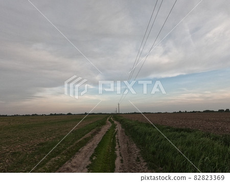 Dirt road among the field. A country road stretches into the distance among the fields. Evening landscape. Dirt road among the field. A country road stretches into the distance among the fields. Evening landscape. 82823369