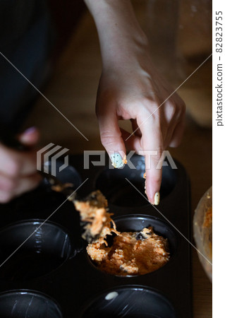 The girl spreads the dough with her finger in a form for muffins with pumpkin 82823755