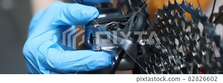 Gloved handyman repairs rear cassette of bicycle 82826602