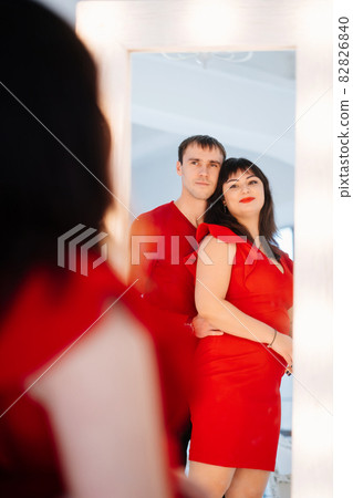 an attractive chubby woman in a red dress with a man looks in the mirror.  82826840