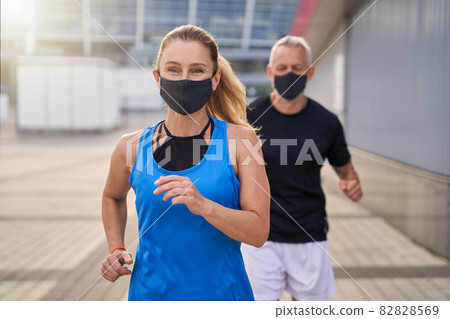 Motivated sportive woman wearing protective mask while running together with her husband to stay fit during Covid19 pandemic Motivated sportive woman wearing protective mask while running together with her husband to stay fit during Covid19 pandemic 82828569