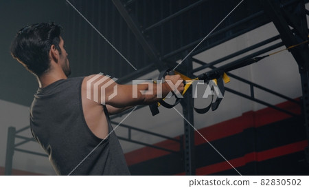 Muscular man during exercise training workout bodyweight with suspension straps TRX 82830502