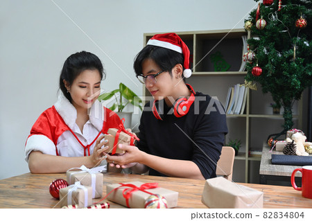 Happy young couple opening Christmas gift in living room at Christmas time. Happy young couple opening Christmas gift in living room at Christmas time. 82834804
