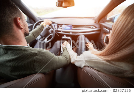 Top view of pair in love in cabin of luxury car. Man driver and his girlfriend on front passenger seat holding each other's hand tightly. Romantic moments of two lovers while riding automobile. Top view of pair in love in cabin of luxury car. Man driver and his girlfriend on front passenger seat holding each other's hand tightly. Romantic moments of two lovers while riding automobile. 82837136