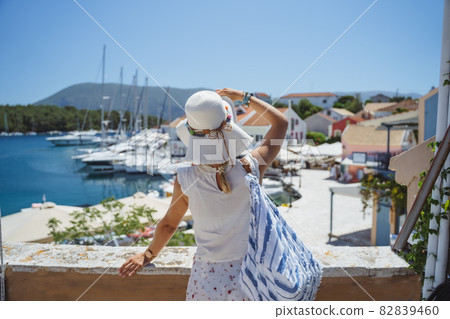 A tourist woman with hat enjoy view of idyllic village of Fiskardo, Kefalonia, Greece, during summer vacation time A tourist woman with hat enjoy view of idyllic village of Fiskardo, Kefalonia, Greece, during summer vacation time 82839460