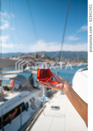 Woman holding glass of wine against yachts at the harbor of Poros. Greece 82841501