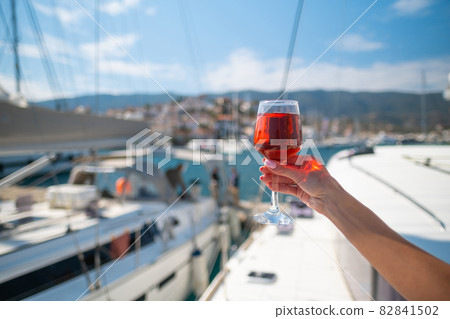 Woman holding glass of wine against yachts at the harbor of Poros. Greece Woman holding glass of wine against yachts at the harbor of Poros. Greece 82841502